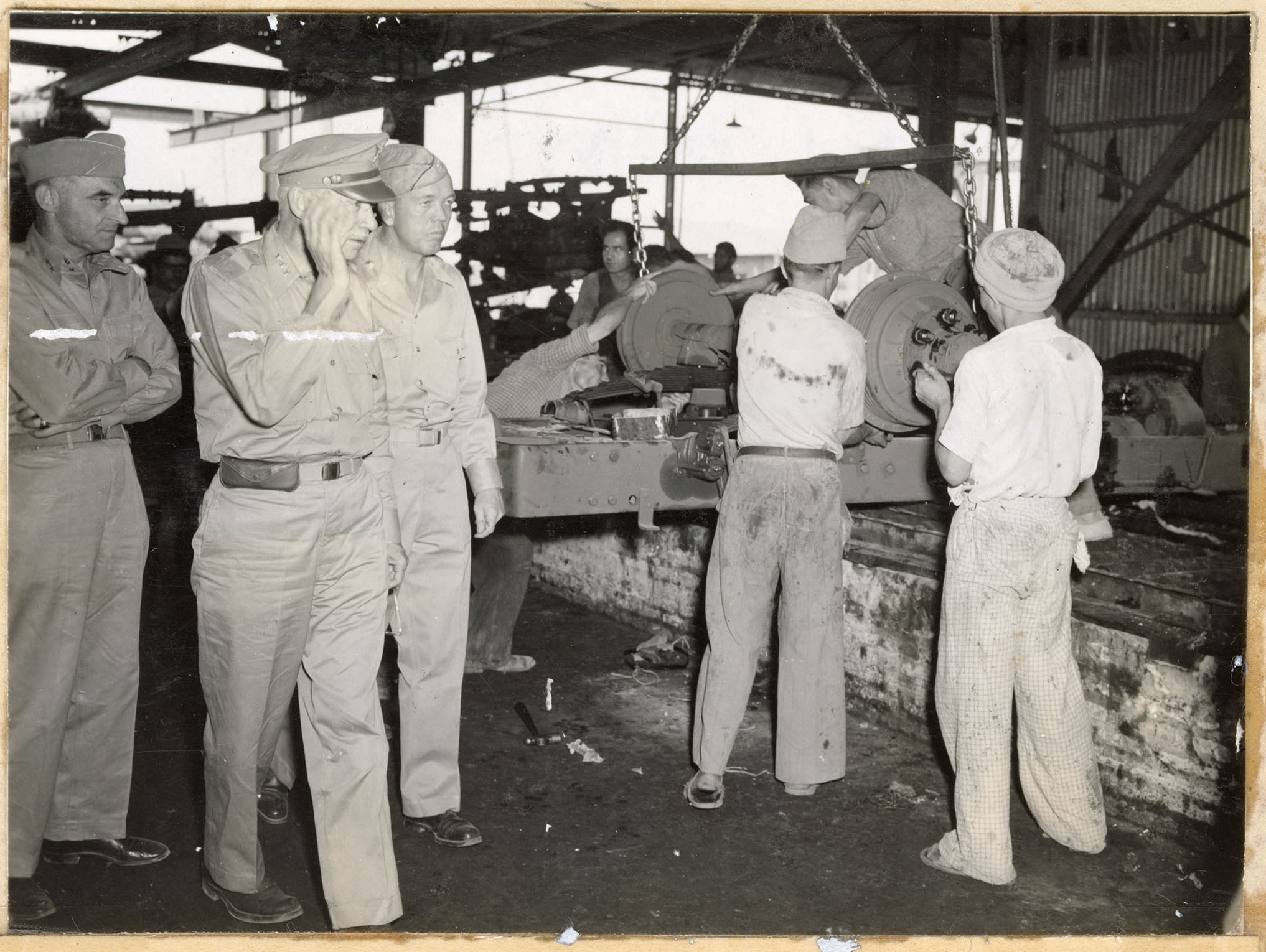 Three US officers walk by Iranian workers in a factory Three US officers walk by Iranian workers in a factory